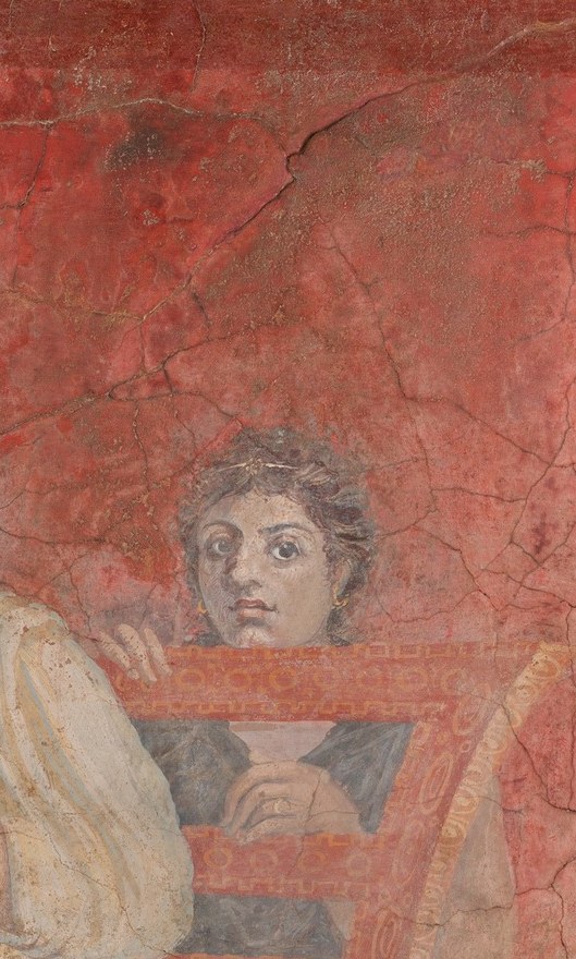 Her smaller scale and position behind the chair suggest attendant or pupil status; her gaze toward the viewer breaks the scene's self-containment and implicates us as witnesses.