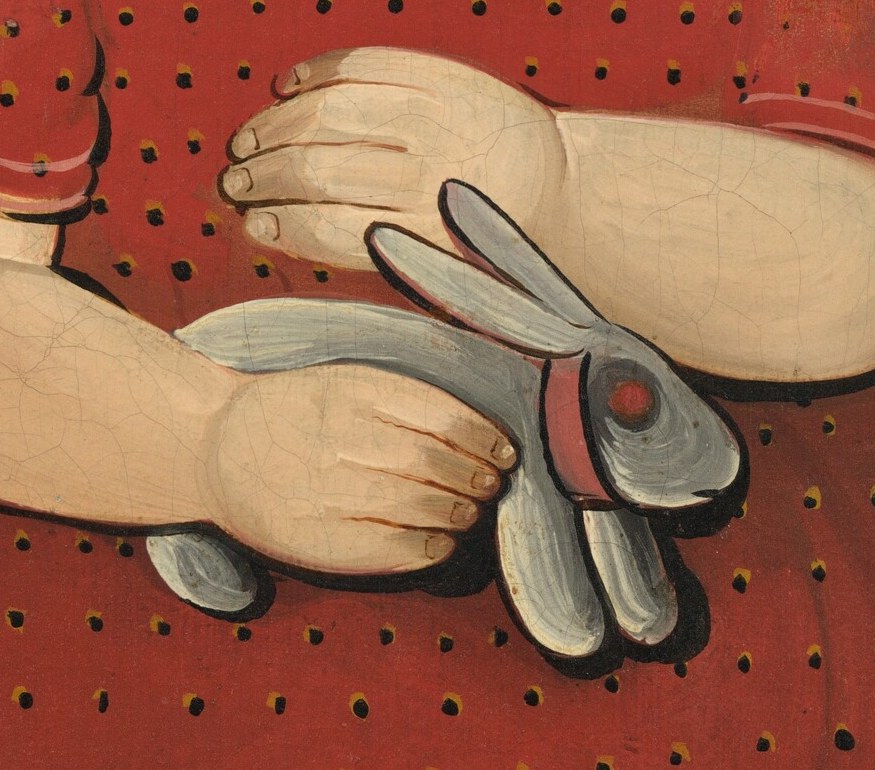 The way her hands cradle the toy rabbit reveals a tender, childlike attachment and provides a focal point for her interaction with an object.