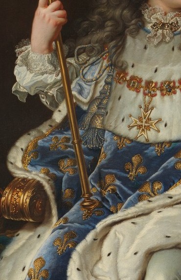 His tiny hand grips a scepter taller than he is.