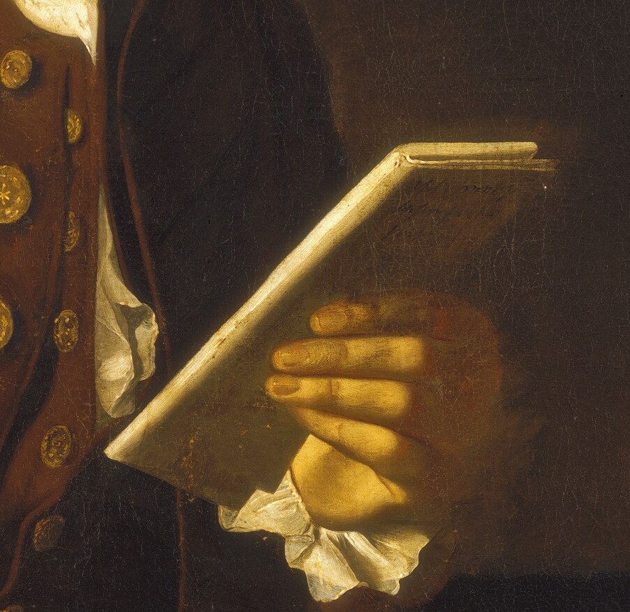 He holds an open book, a sign of his learning and literacy.