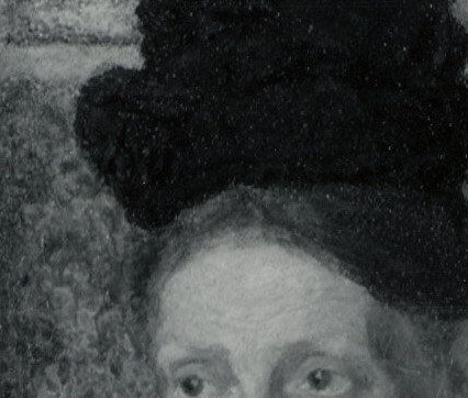 The hat frames her face and adds a somber, formal element to her attire.