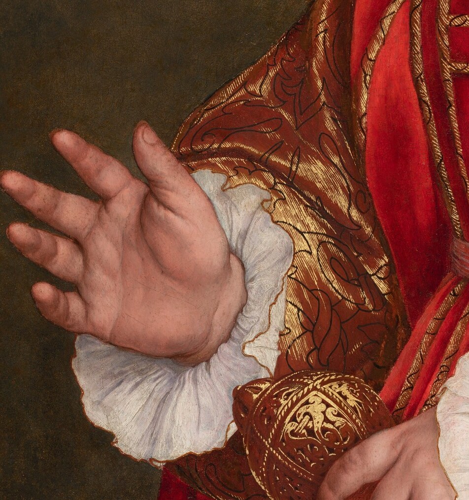 His raised hand borrows the gesture of a papal blessing.