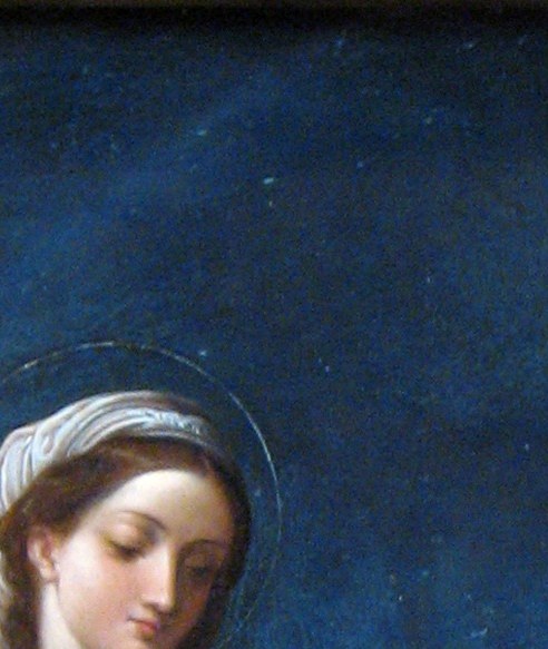 Her gentle downward gaze and soft illumination convey maternal tenderness; the most emotionally legible face in the composition.