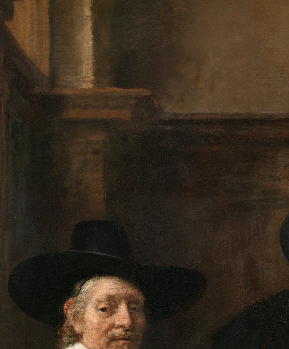 Direct gaze at the viewer; slightly shadowed, he anchors the left edge and creates the sensation the viewer has walked in on a working session already in progress.