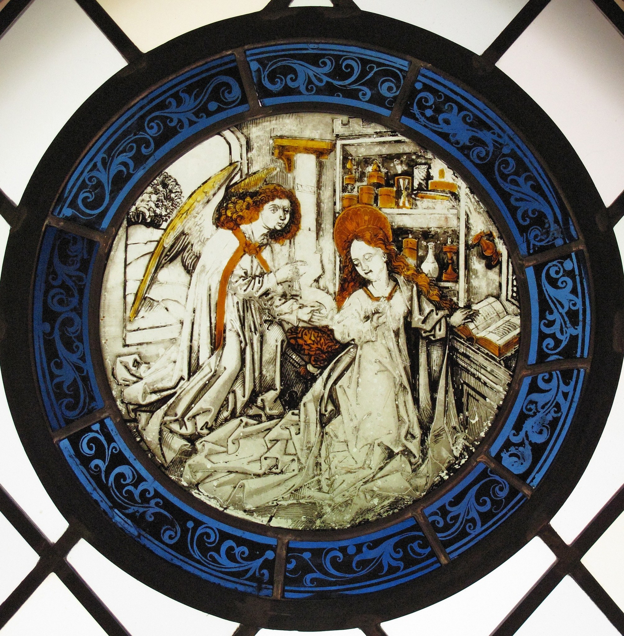 The cobalt blue ring with white scroll-work is a distinctive feature of the roundel format; its ornamental vocabulary dates the piece and signals its function as architectural glazing.
