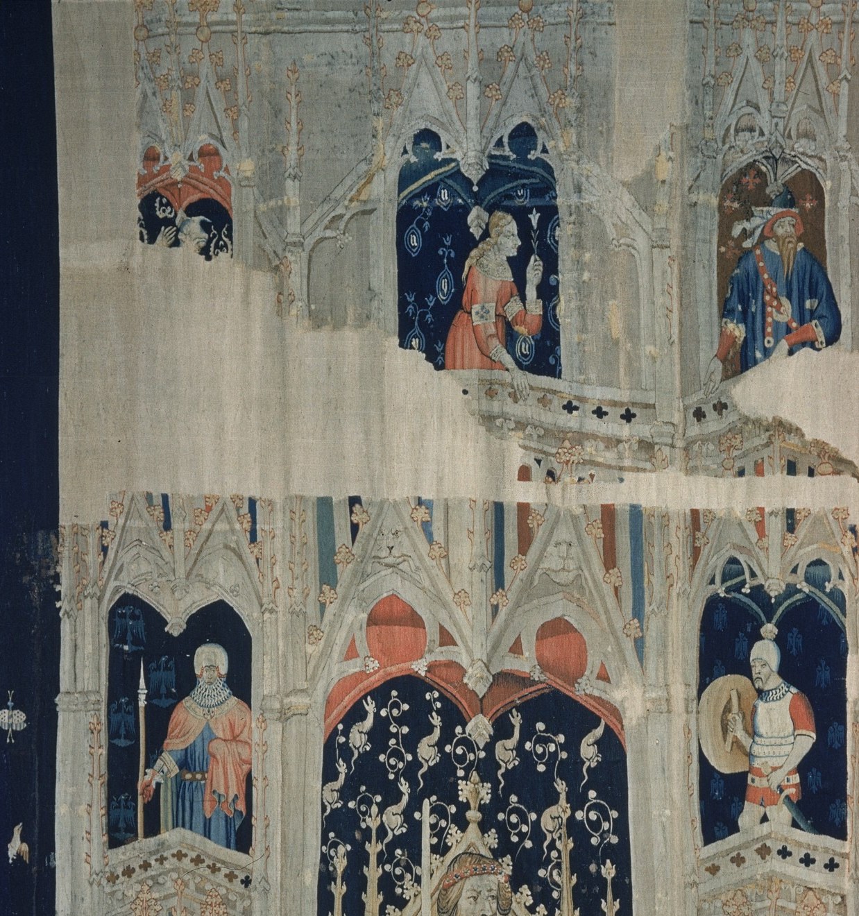 The architectural tracery is the tapestry's structural and aesthetic signature; the quality of the Gothic foliage and pinnacle work is a benchmark of the International Gothic weaving workshop