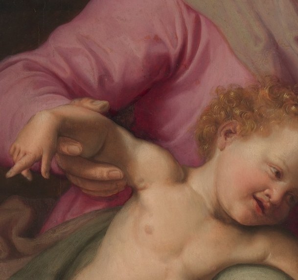Soft infant features tilted down toward the lamb; the downward orientation echoes the sacrificial theme without explicit drama.