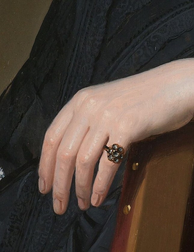 The relaxed pose of her hand suggests ease and confidence, resting on the rich texture of the chair.