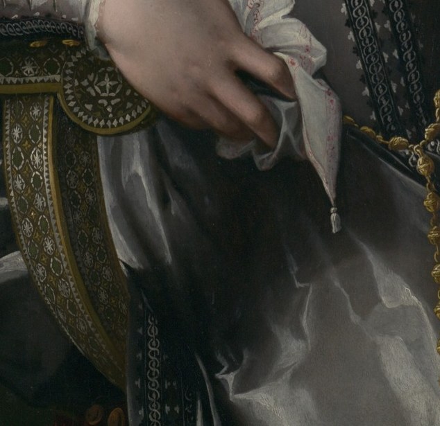 Gloves held, not worn. She has never lifted anything heavier than a goblet.