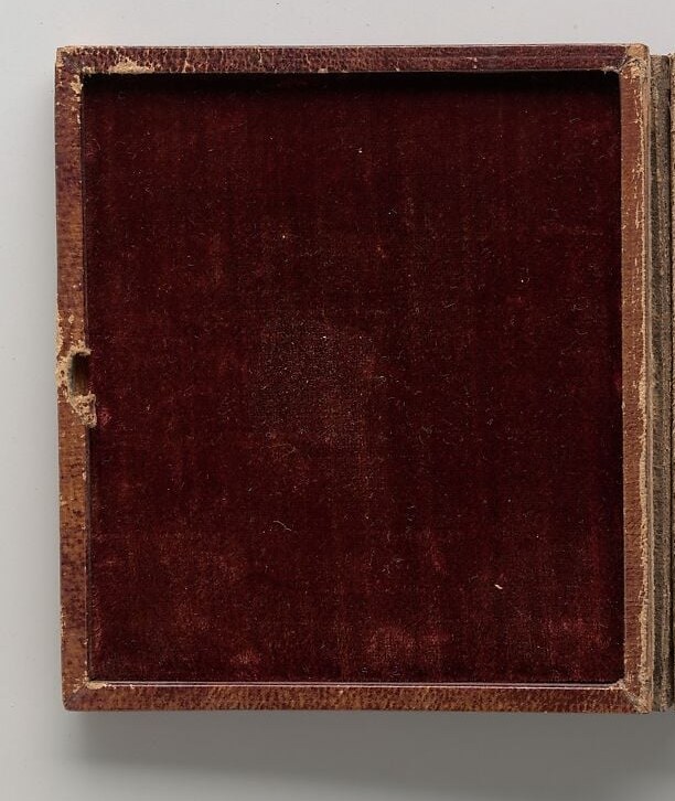 Reveals the object's identity as a portable keepsake meant to be held, not hung; the lining's rich red frames the entire viewing experience and survives better than the ivory in the image.