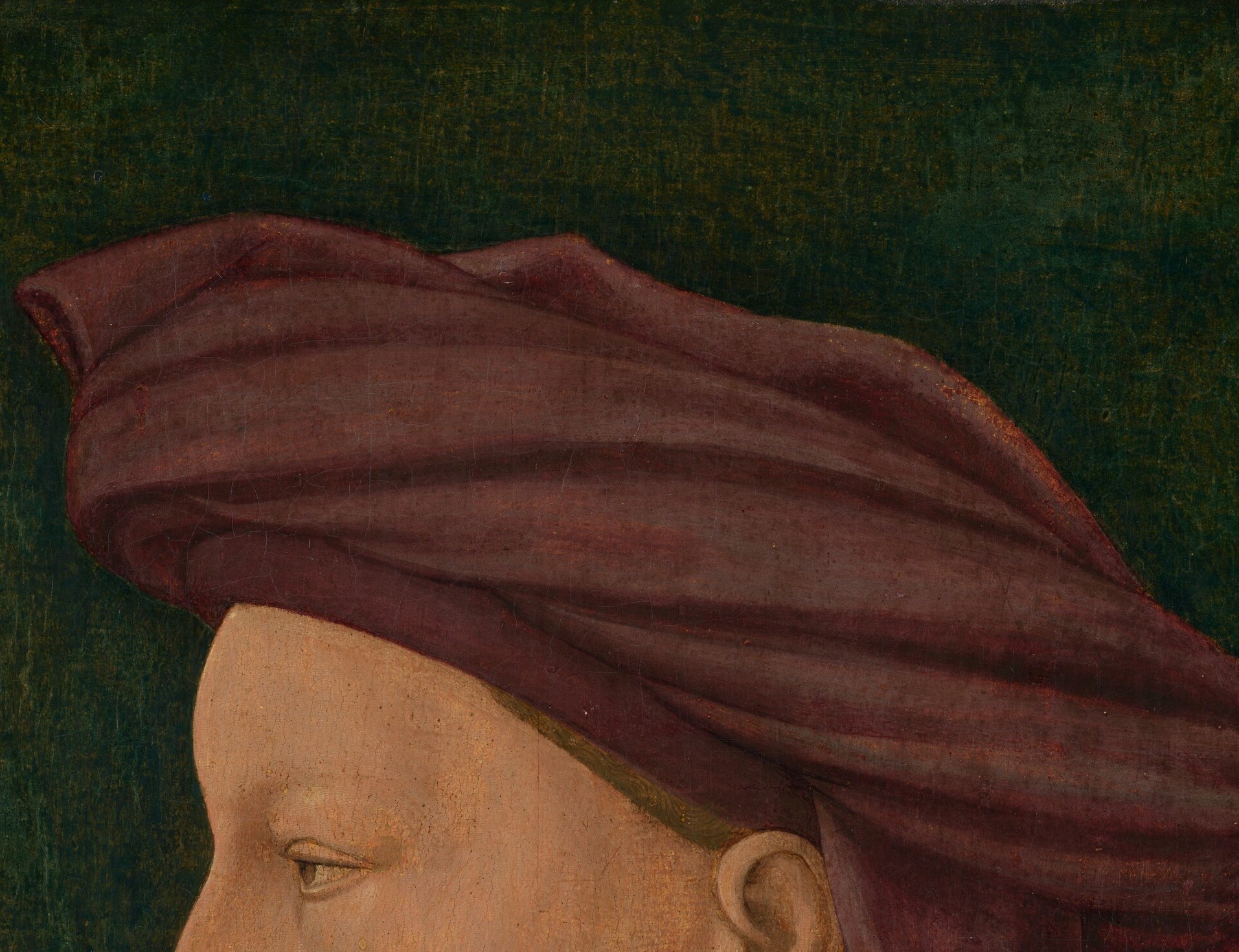 The chaperon is the status badge: its deep rose-red pigment and sculptural fold identify the wearer as a young Florentine of means; the tail spills behind the skull as a social signal