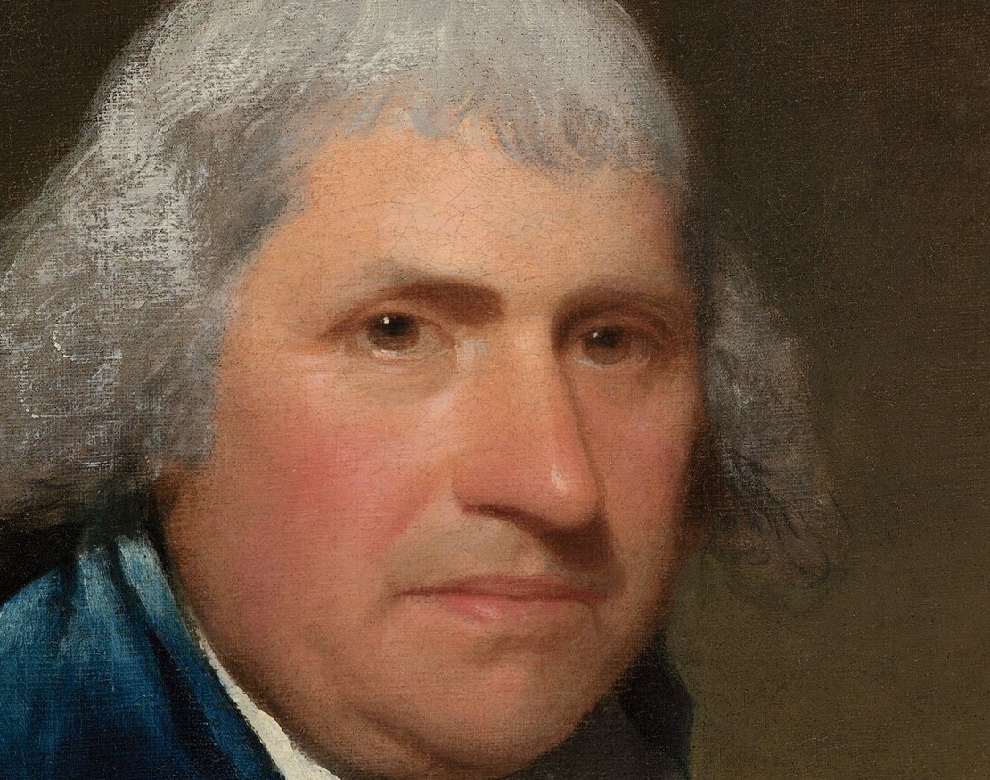 The crisp white linen against the dark coat creates the brightest value anchor below the face, drawing the eye downward in a deliberate compositional rhythm.
