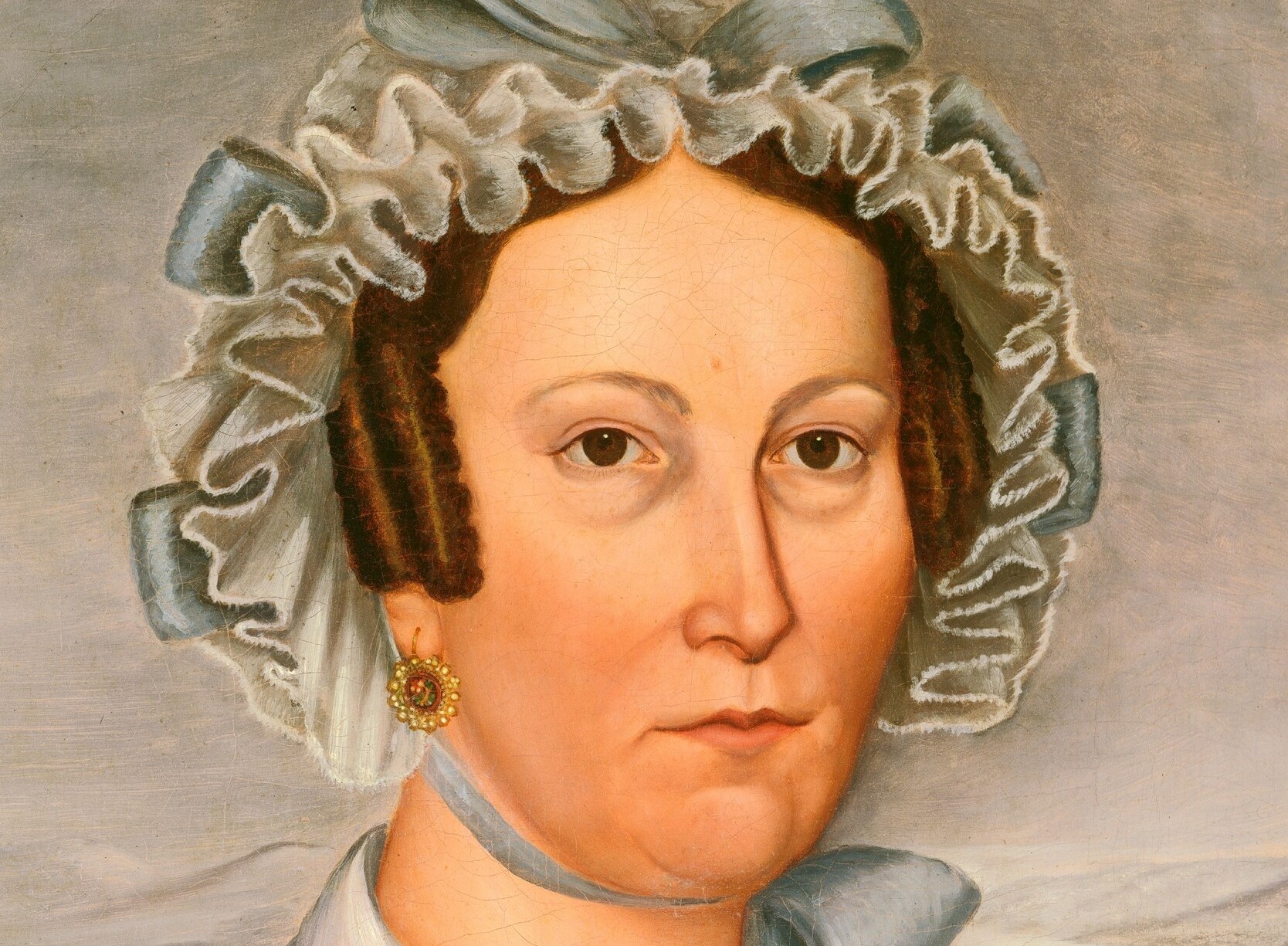 The elaborate bonnet, with its ruffles and ribbon, is a testament to the fashion and social status of the era.