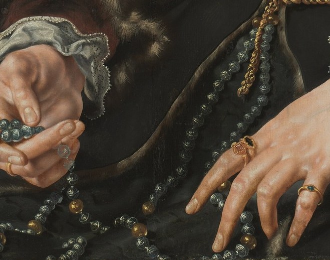 Her hands hold a rosary and a ring.
