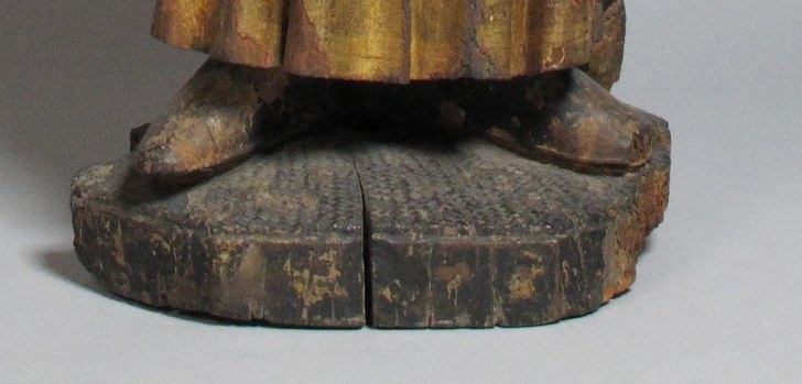 The base is crudely carved and shows significant wear, grounding the figure and emphasizing its age and material.