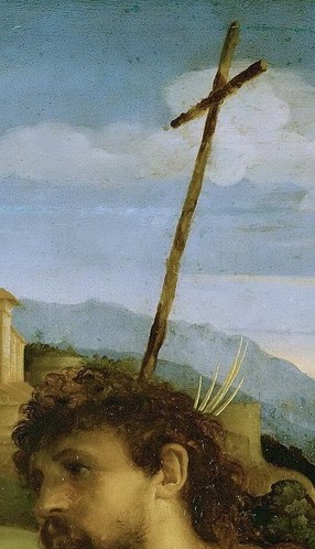 The kneeling man holds a cross made of reeds.