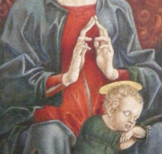The eyes are downcast. The hands pray toward her own child.