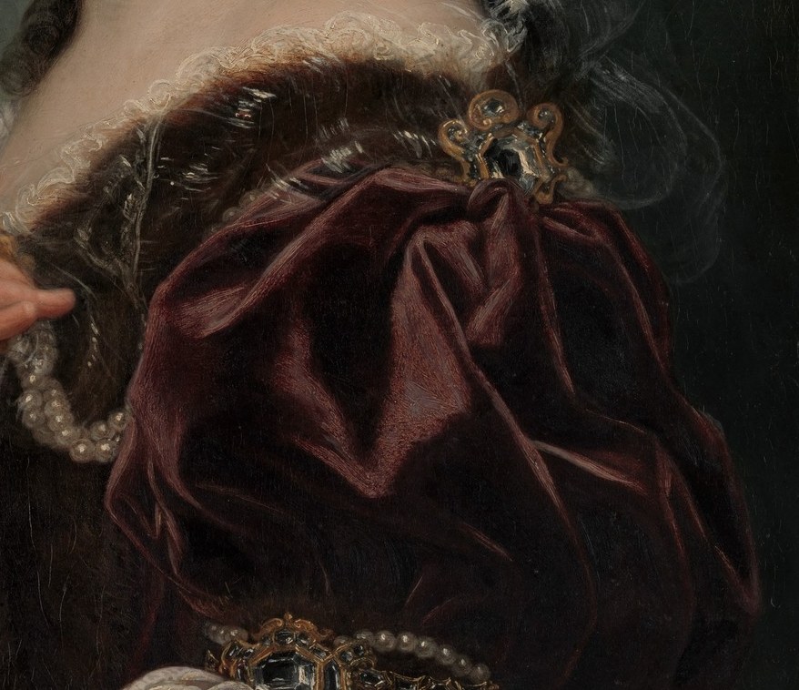 Her rich velvet dress and many jewels signal wealth.