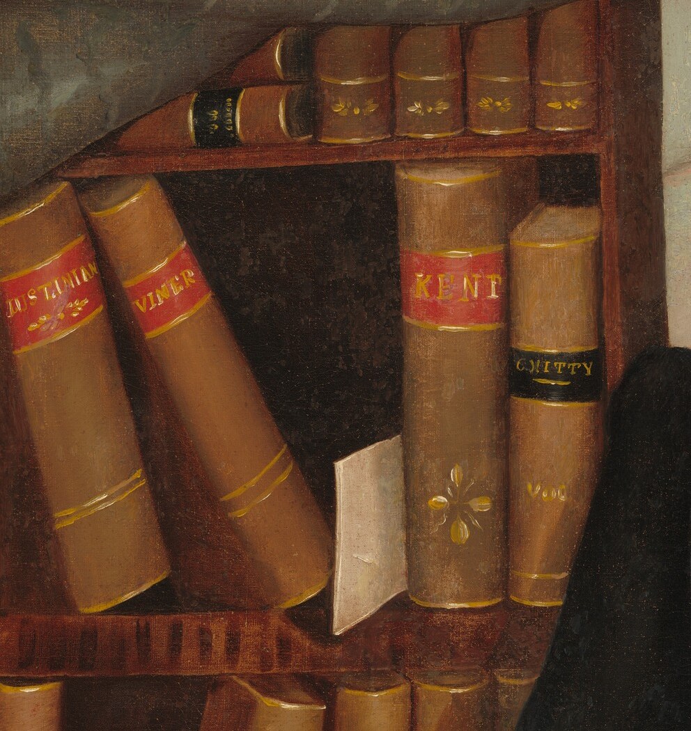 Behind him, rows of leather-bound law books.