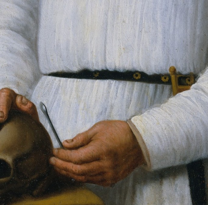 He holds a human skull: the ultimate professional credential.