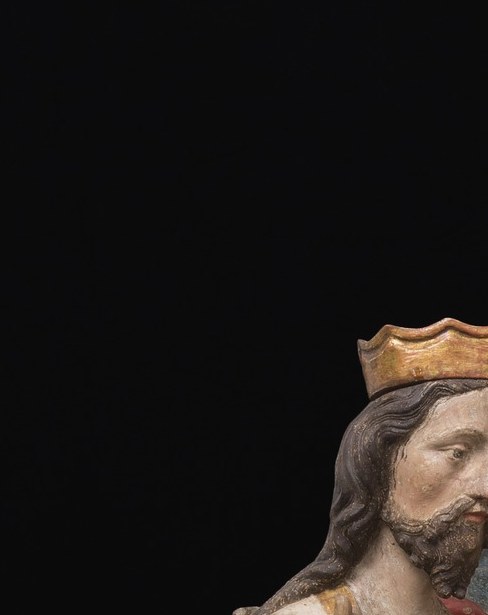 Younger and softer than the central face, this figure embodies the human aspect of the Trinity; its crown is smaller, encoding the Trinitarian hierarchy in metal.