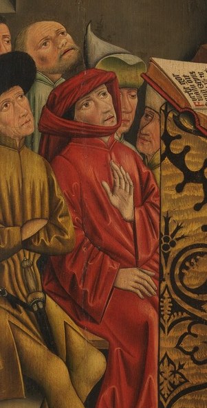 A man in red listens with clasped hands.