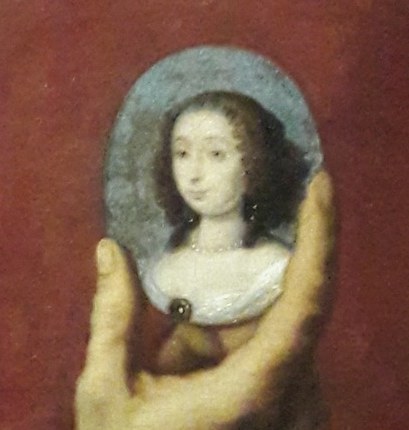 He holds a miniature portrait of a woman.