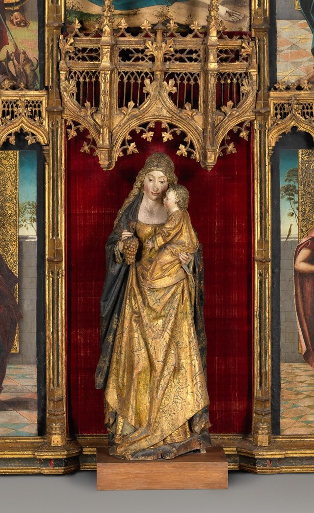 The most richly dressed figure in the whole work , the gilded vestments signal either the Virgin in glory or a powerful interceding saint; her placement at the base draws the eye.