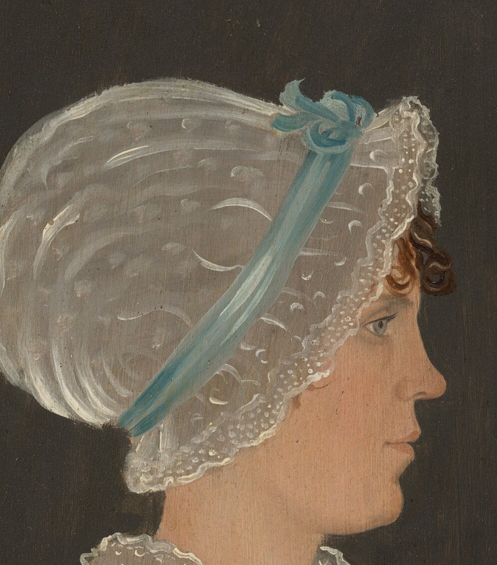 The delicate lace and sheer fabric of the bonnet suggest refinement and fashion of the era.