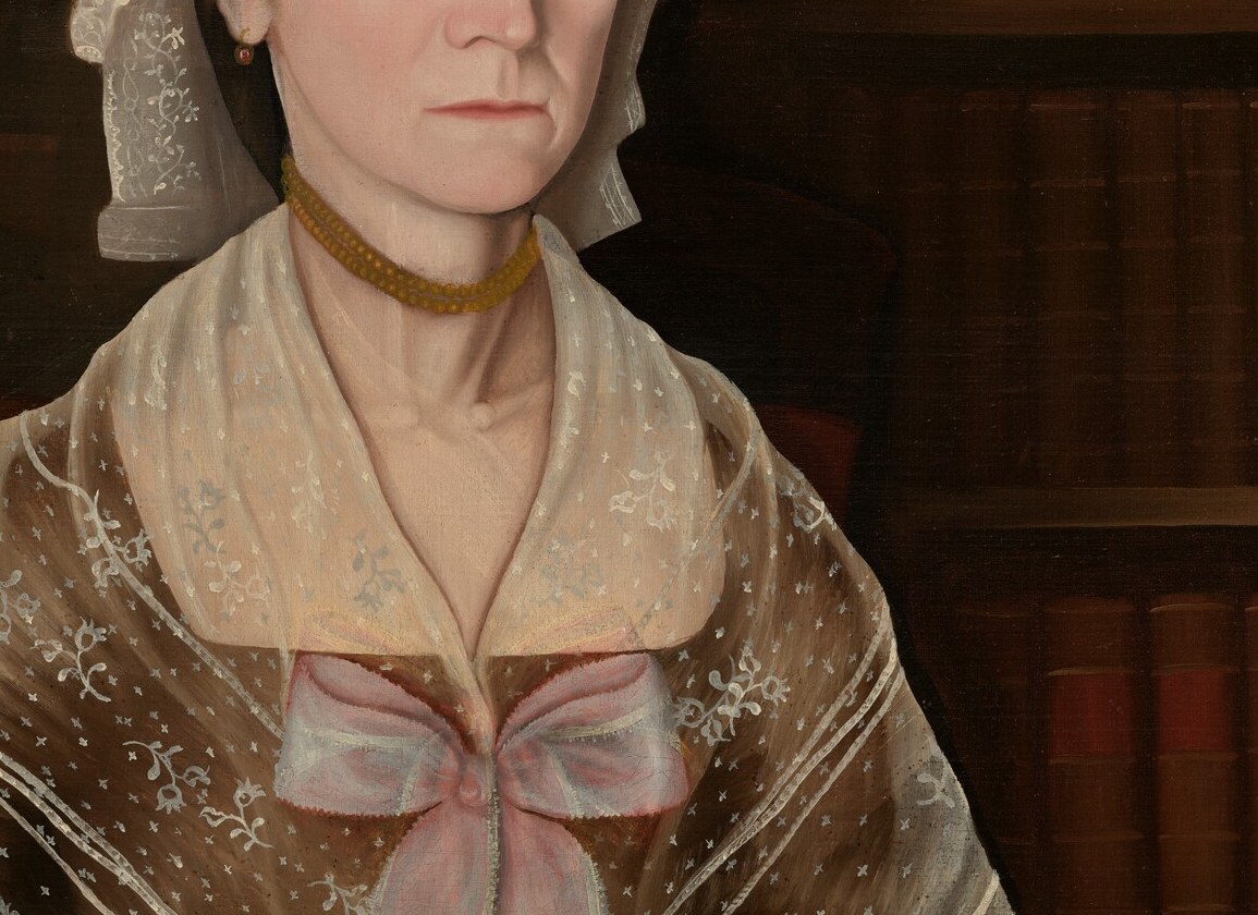 The triangular collar of fine white lace softens the neckline and marks the sitter's gentility; the contrast of lace against the dark gown draws the eye toward the pendant.