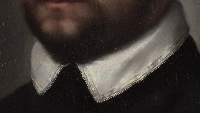Its sharp pleats and bright white contrast with his dark attire, drawing attention to his neck and face.