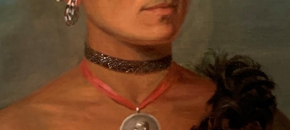 Around his neck, shell and metal ear ornaments. Beside them, a layered bead choker.