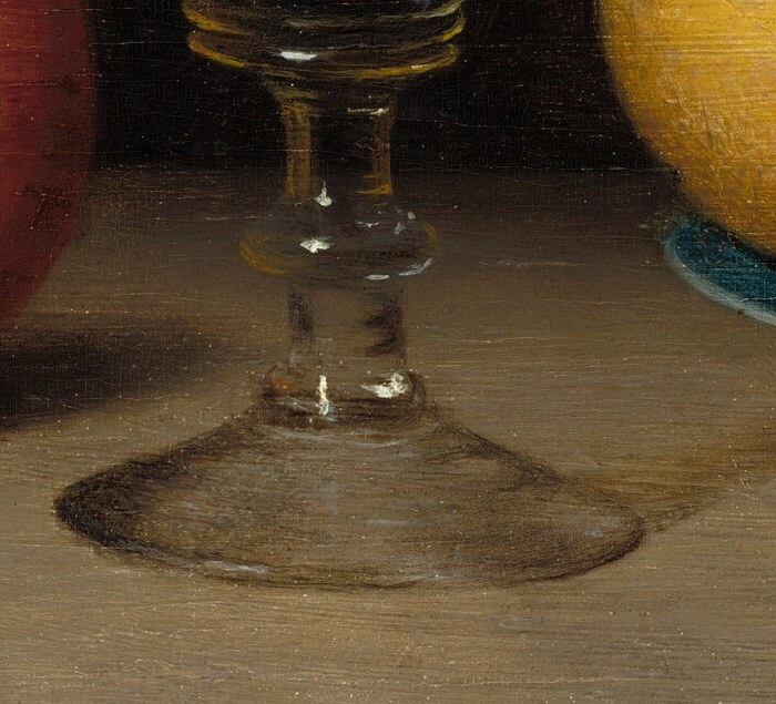The faceted stem holds a reflection of the shelf and the dark room.