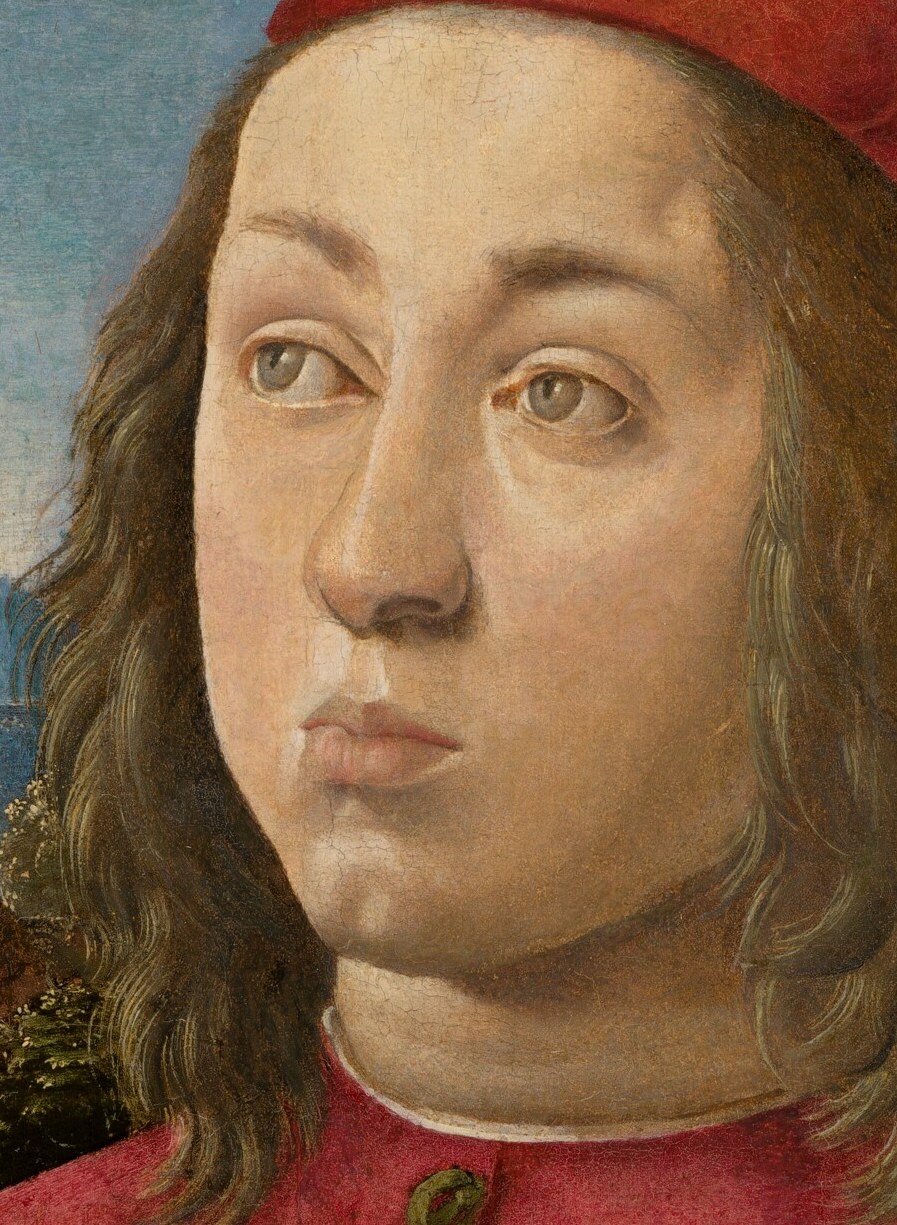 His long, flowing hair and red cap frame his young face.