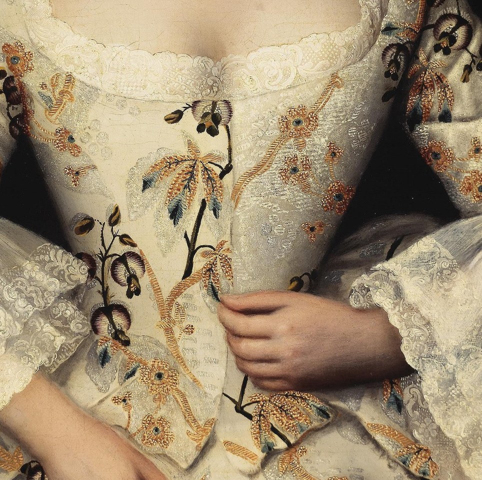 Her bodice, richly embroidered with floral motifs, signals fashion.